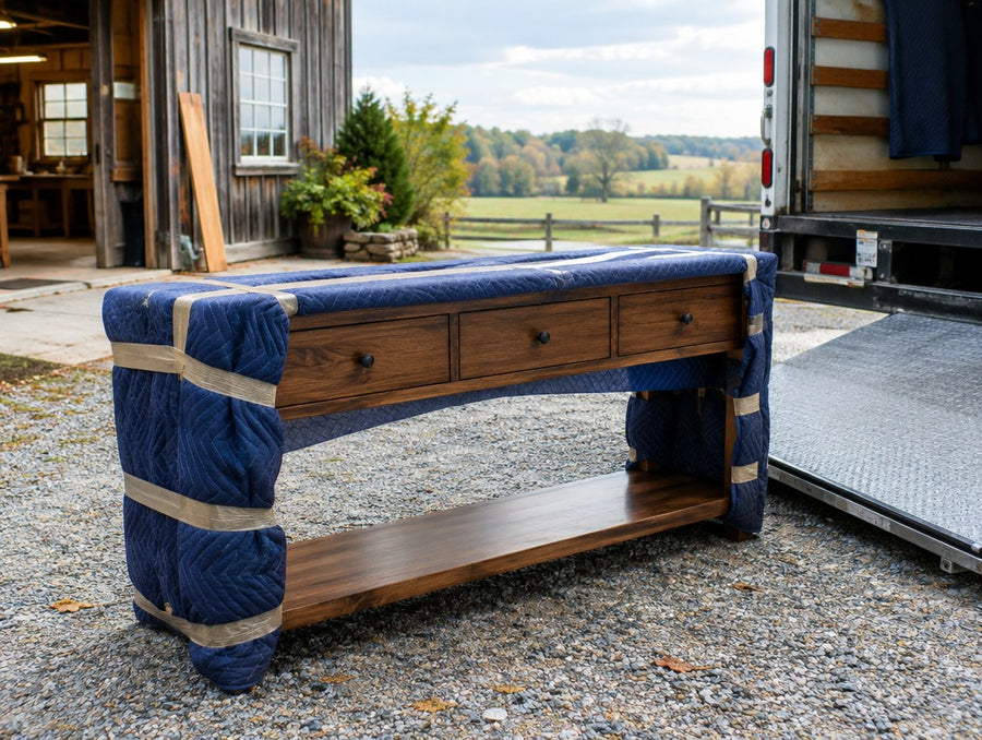 A blanket-wrapped console table carried to a delivery truck outside a rural Ohio workshop